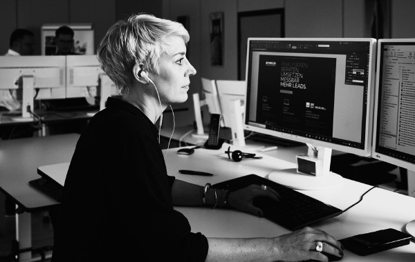 DIE MARKETING AGENTUR arvenio Mitarbeiterin Patricia Deuring sitzt vor zwei Bildschirmen mit Grafikprogramm geöffnet
